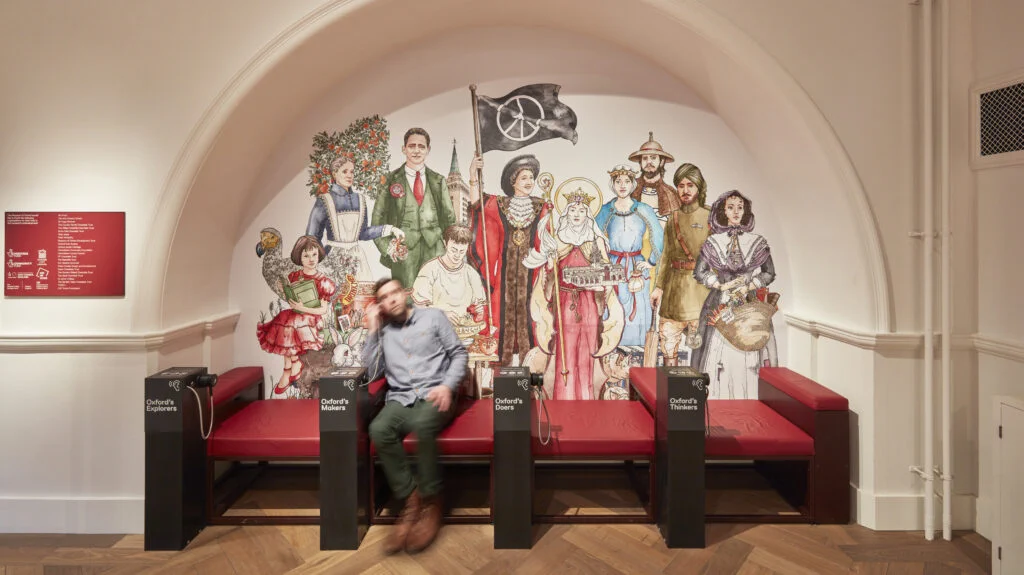 A person sits on a bench in front of a mural of Oxford people at the Museum of Oxford