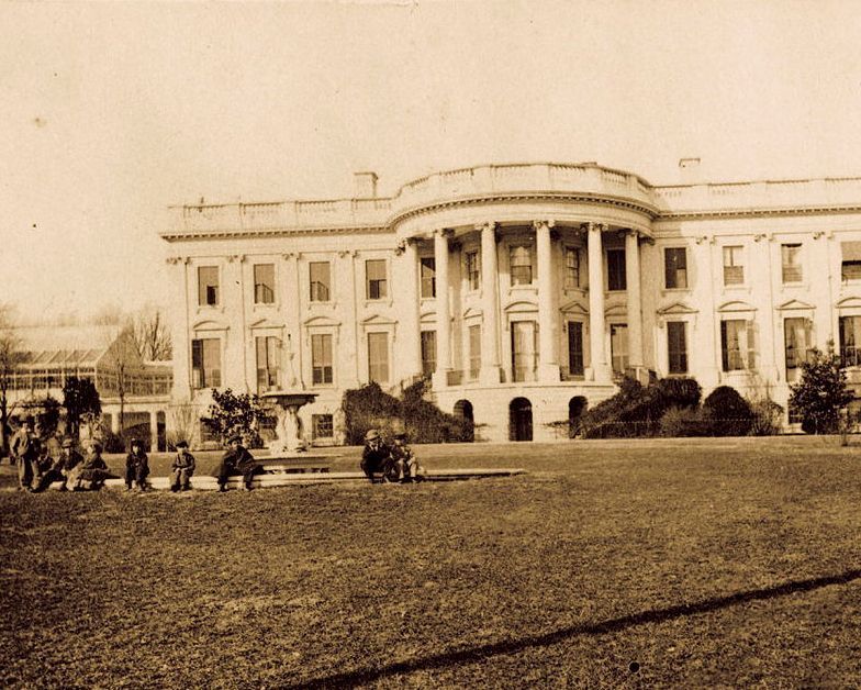 historycalendar's tweet image. This photograph shows the White House with children sitting on the fountain. One of these children is possibly Tad Lincoln. c. 1861-1865.