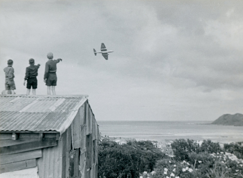 Boys on a roof watching an aircraft, near Rongotai Terrace, Rongotai, Wellington (most likely a visiting R.A.F English Electric Canberra), ca. 1950s. Photographer - Ron Cameron. Source: Wellington City Collect. wellington.recollect.co.nz/nodes/view/8519