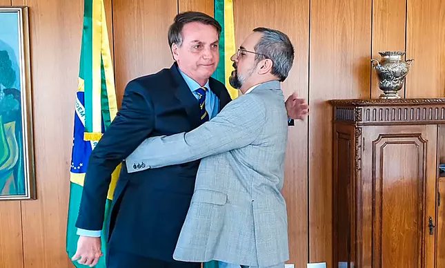 Essa imagem é desconfortável porque ela não é um abraço. É uma tentativa de narrativa.

Jair Bolsonaro aparece rígido, corpo travado, braços baixos, expressão fechada. Não há reciprocidade no gesto. Não há acolhimento. O tronco não avança, o rosto não relaxa, o olhar não sorri. É