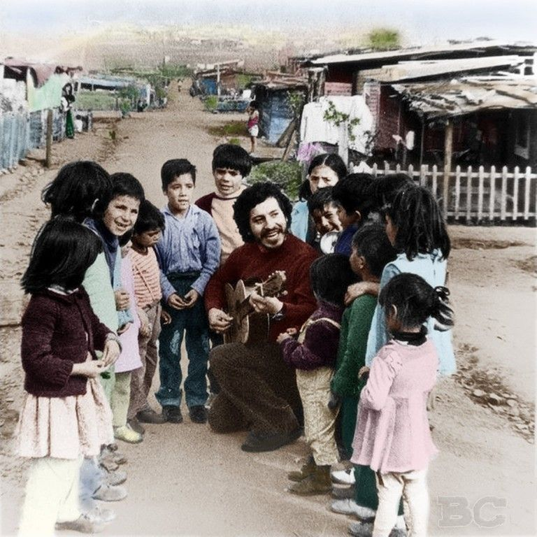 Víctor Jara playing the guitar and singing with children in a shantytown.
