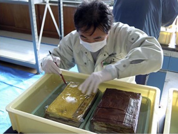 薬液に１時間浸漬させたものを、容器に移し、筆で表面に付着した土砂を丁寧に落としました。その後、慎重に分離させていきました。被災の状況は一様ではなく、割とすんなり離れるものもあれば、なかなか離れないのもありました。見た目が同じでも全く状態が異なるのが津波被災資料の難しさです。