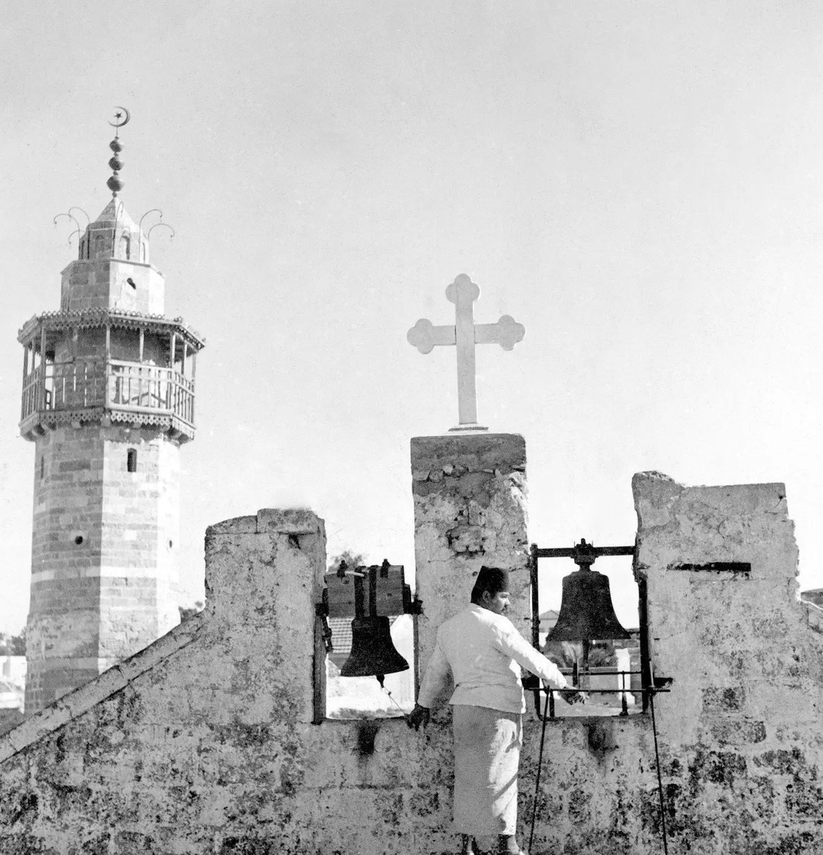 1934, Gaza, Palestine 🇵🇸 

This historical photo, titled "The Cross Embraces the Crescent", captures a moment of religious coexistence in Gaza in 1934. 

It shows the sexton of the Greek Orthodox Church of Saint Porphyrius ringing the church bells, with the adjacent Katib