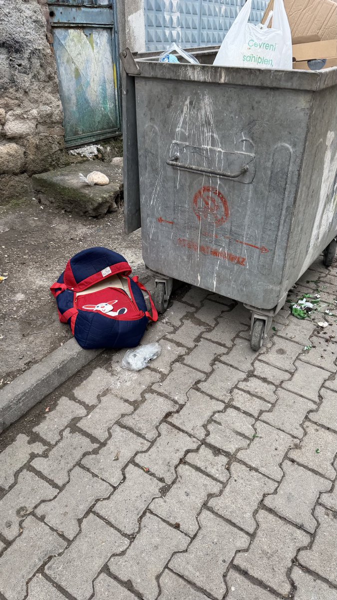 Bir çöp konteynerinin yanında bırakılmış bebek çantası. Öyle bir dönemdeyiz ki, insan uzaktan bakıp içinin dolu olmadığını kendine telkin etmek zorunda kalıyor.