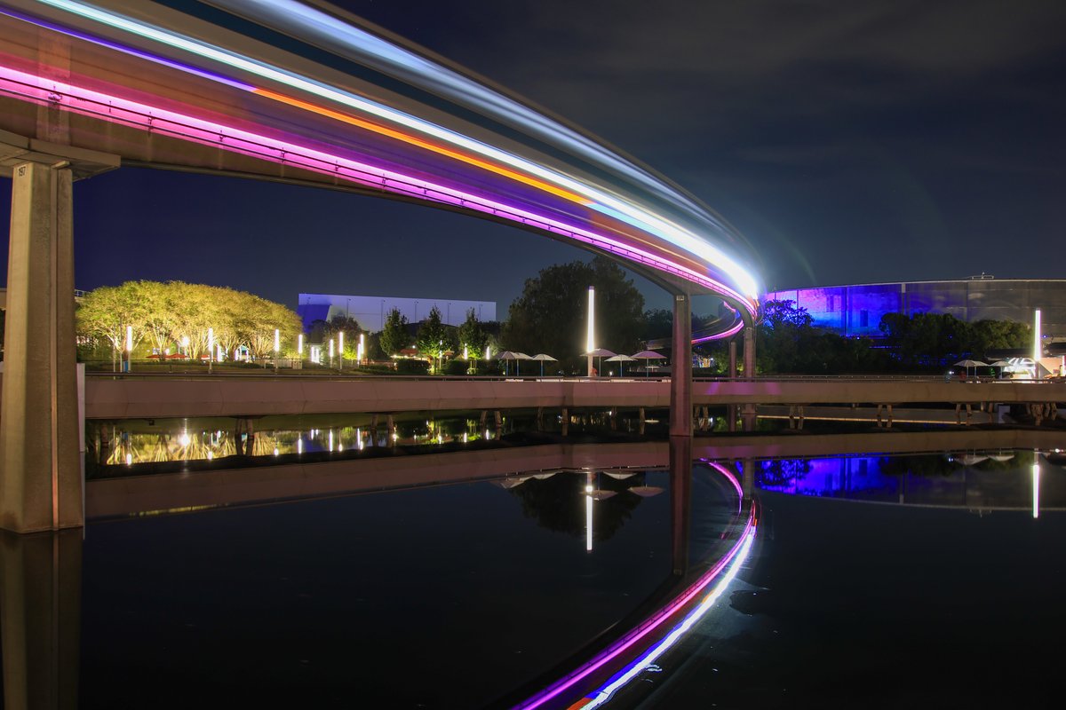 bioreconstruct's tweet image. Mirror glass reflection of a monorail train in EPCOT. Under carriage lighting changing from orange to purple. 14s long duration photo.