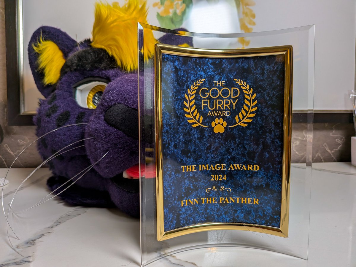 Finn's purple and yellow fursuit head behind a plaque reading "The Good Furry Award. The Image Award 2024. Finn the Panther!"