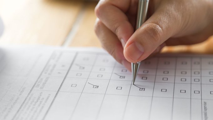 A hand holding a pen, making checkmarks on a piece of paper.