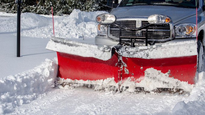 Un camion équipé d’un chasse-neige déneige une entrée de cour.