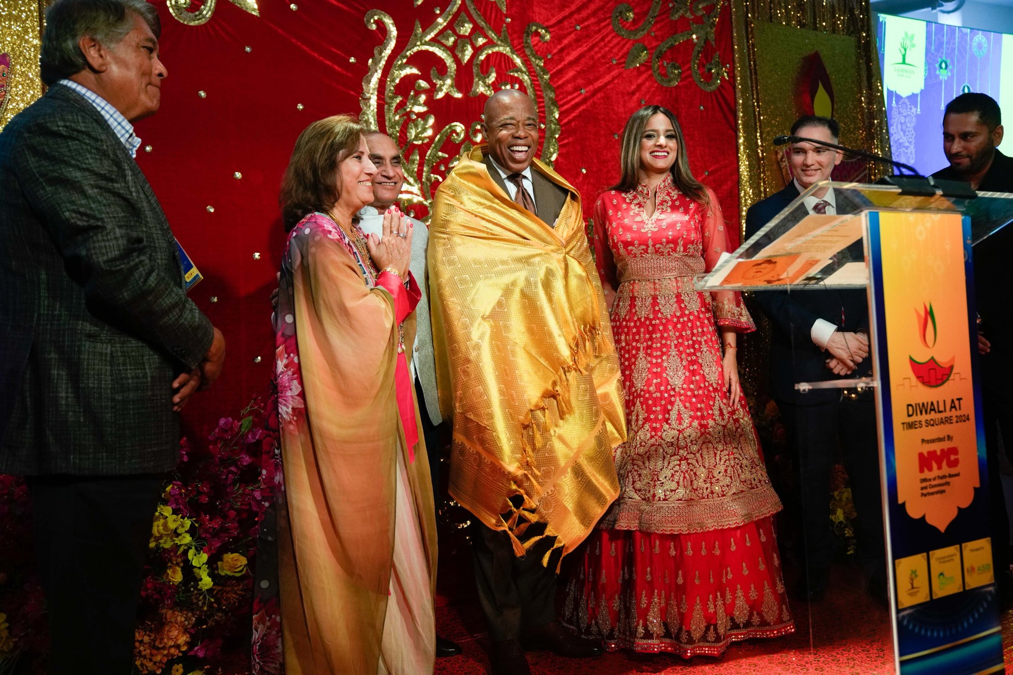 Mayor and Diwali at Times Square organizers stand on stage with mayor wearing ceremonial gold fabric around him