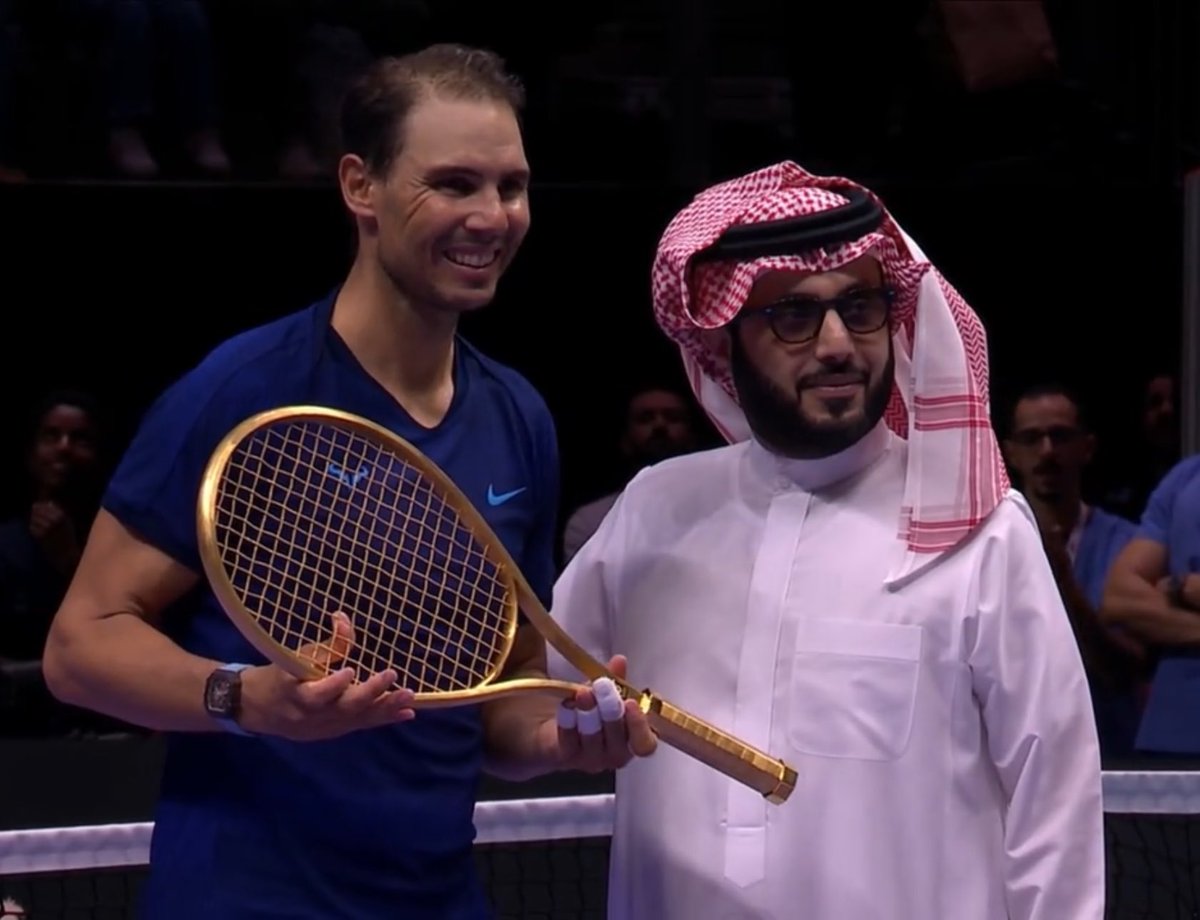 FonsiLoaiza's tweet photo. Rafa Nadal se retira del tenis jugando en un torneo por 1,5M€ en Arabia Saudí, dictadura de la que es embajador. Recibe como premio una raqueta bañada en oro por uno de sus jeques. Prepara su jubilación de oro como socio inmobiliario de un fondo buitre con los Matutes. https://t.co/uFHb82bbEz