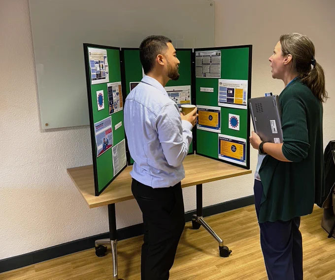Two people are talking in front of a poster board.