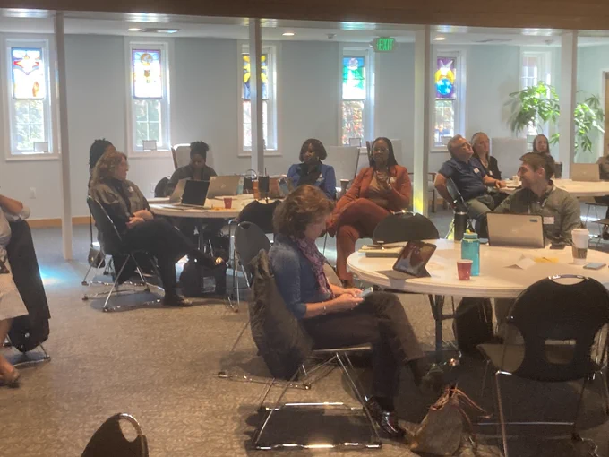 Photo of the meeting room. Meeting attendees are sitting at round tables.