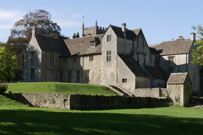 A view of Horton Court from the garden. The stone house rises out of a well-kept lawn against a blue sky. 