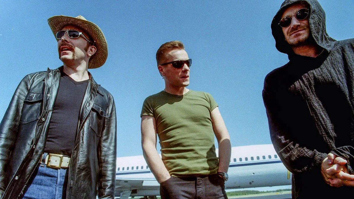 U2ThreeChords's tweet photo. Edge, Larry and Bono photographed with the Popmart tour plane in the background. 🪩🛒 https://t.co/O0Jicxr44Z