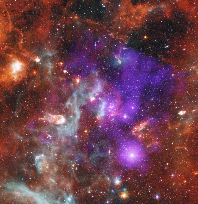 The Cygnus OB2 star cluster resembles a night sky blanketed in orange, purple, and grey clouds. The center of the square image is dominated by purple haze. This haze represents diffuse X-ray emissions, and young stars, detected by the Chandra X-ray Observatory. Surrounding the purple haze is a mottled, streaky, brick orange cloud. Another cloud resembling a tendril of grey smoke stretches from our lower left to the center of the image. These clouds represent relatively cool dust and gas observed by the Spitzer Space Telescope. Although the interwoven clouds cover most of the image, the thousands of stars within the cluster shine through. The lower-mass stars present as tiny specks of light. The massive stars gleam, some with long refraction spikes. Credit: X-ray: NASA/CXC/SAO/J. Drake et al, IR: NASA/JPL-Caltech/Spitzer; Image Processing: NASA/CXC/SAO/N. Wolk