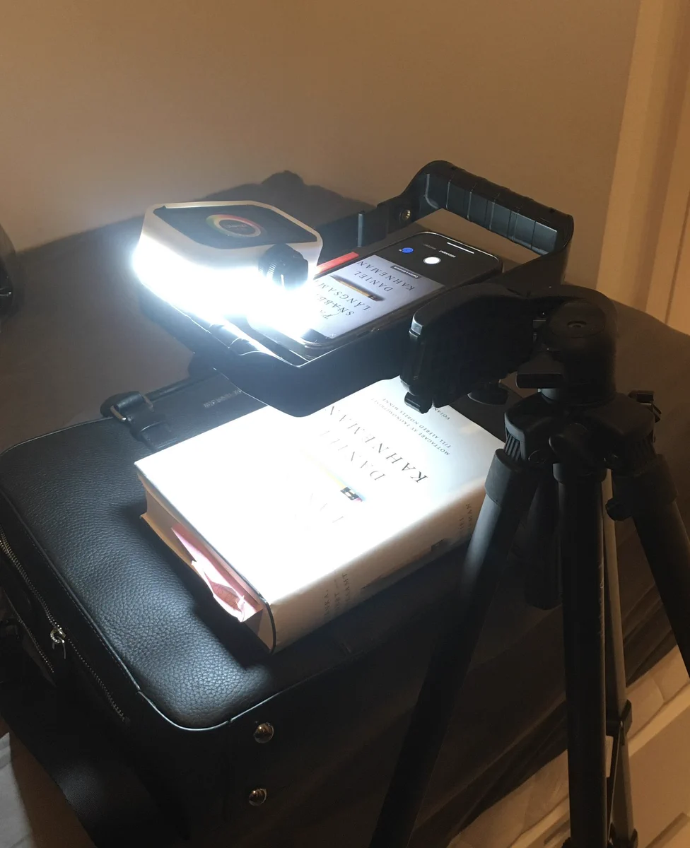 An iPhone on a tripod with a lamp over a black laptop bag. The camera is angeled down to make a simple scanning device for documents