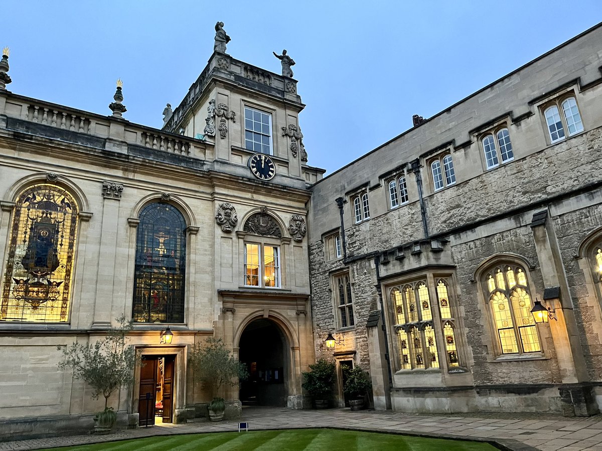 The chapel tower and dining hall of Trinity College with blue sky and lights inside the buildings.