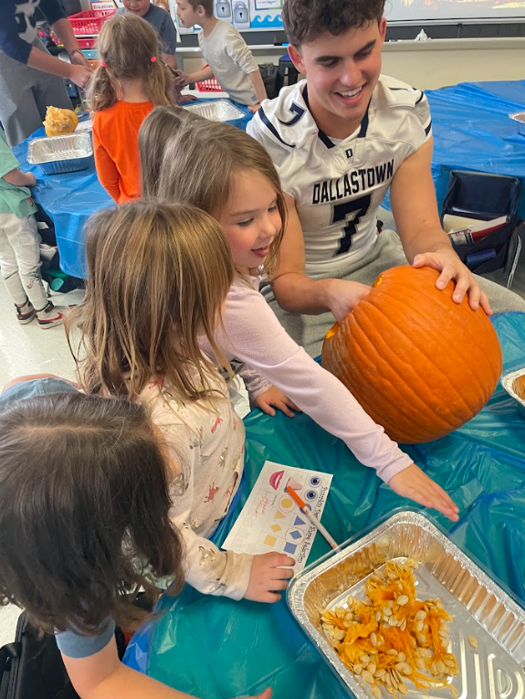 DallastownSD's tweet photo. Pumpkins and pigskin! Our high school football players teamed up with Mr. Andrews' kindergarten class at #YTE for a hands-on pumpkin investigation! It was a field trip in their classroom, blending big-kid leadership with curious, little-kid wonder. https://t.co/0SsbVr9T03