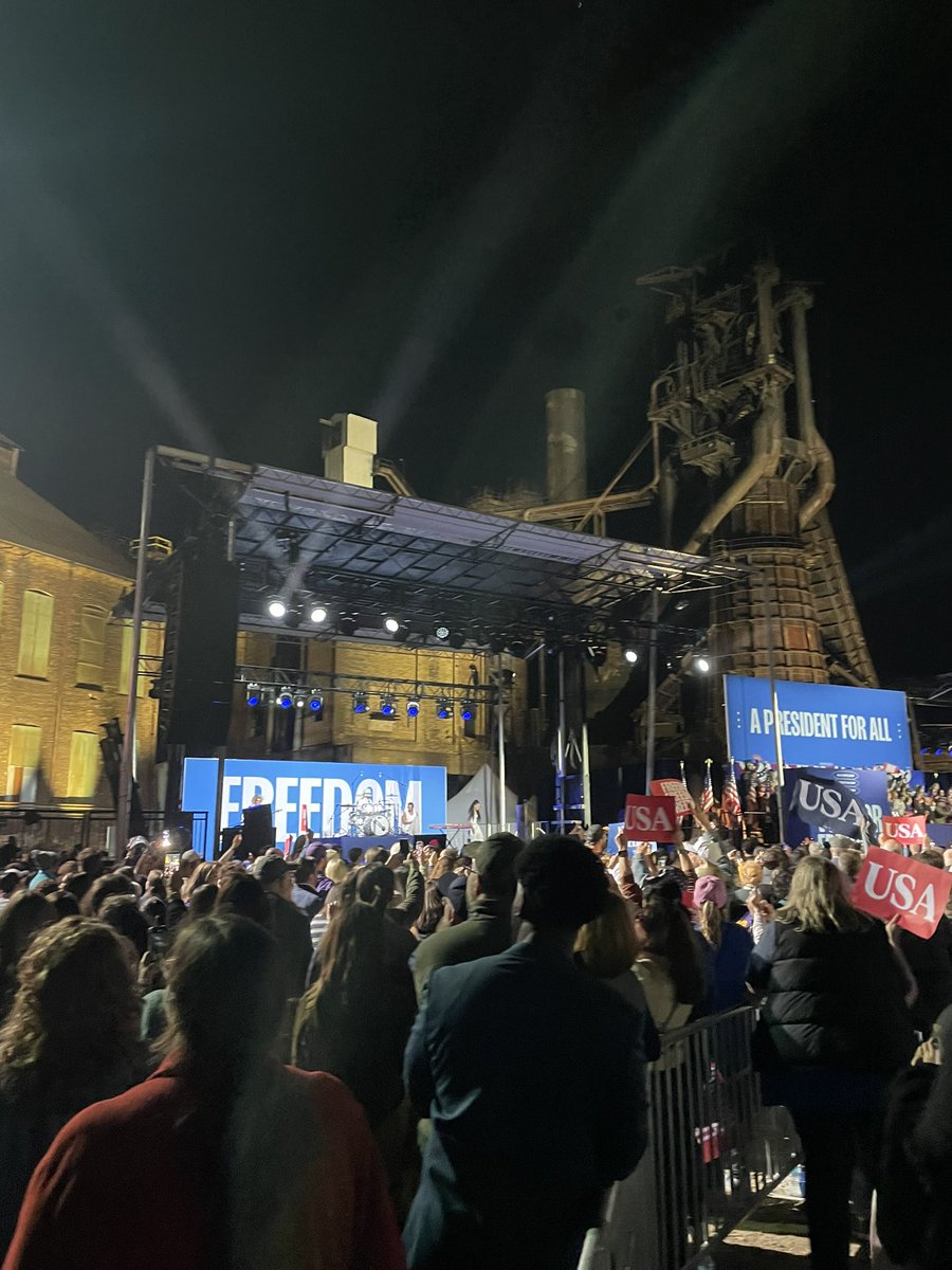 A bat-signal style “Steelworkers for Harris Walz” sign at Harris’ Pittsburgh rally held at a historic furnace site.