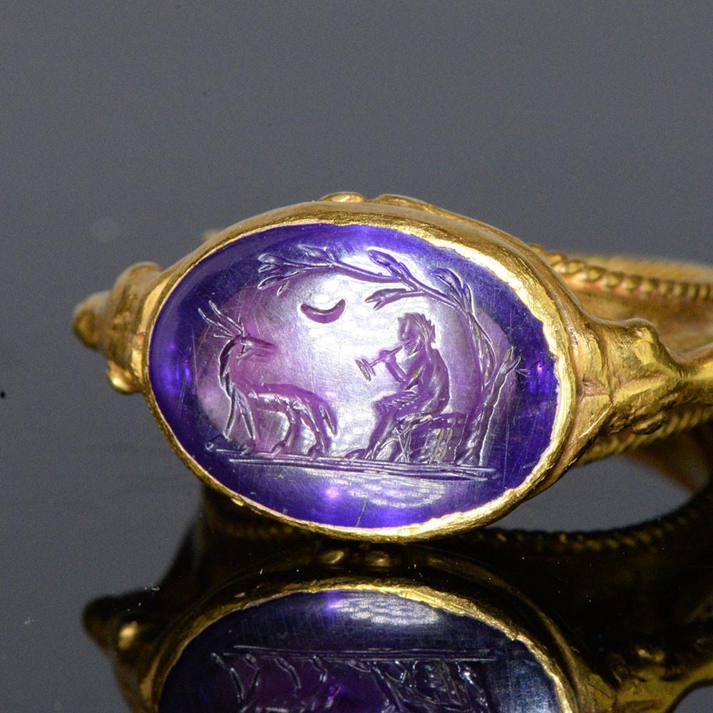 Ancient Roman amethyst intaglio showing Pan, the pastoral god, playing pipes under a crescent moon and a leaning tree, with a goat observing. Dated between the 1st and 2nd centuries AD. The gold ring setting is of a later date. Collection &amp; Credit: Sands of Time Ancient Art.