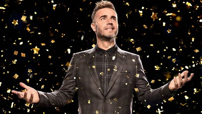 Gary Barlow standing next to his son eating a croissant.