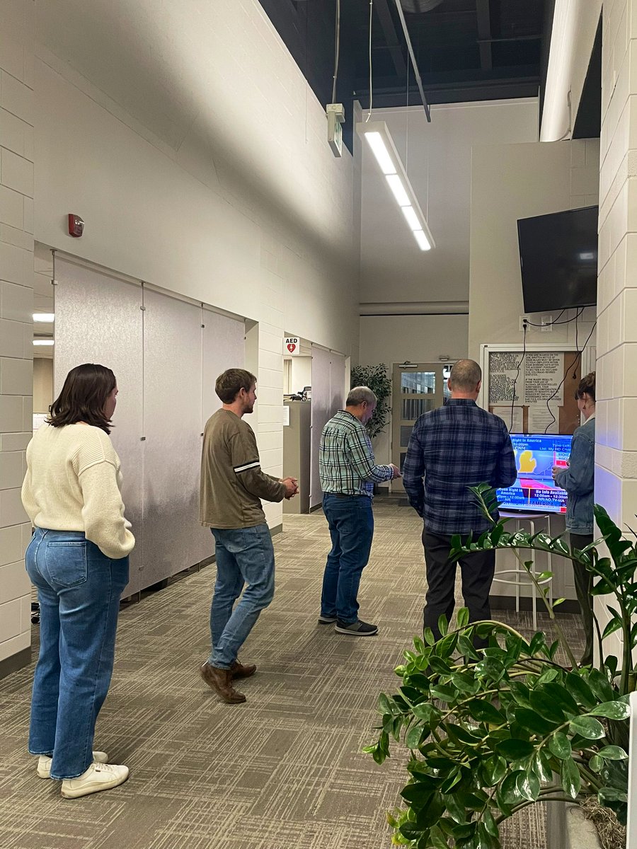 meganululani's tweet image. Here we see @denverpost journos drawn to the newsroom’s sole TV with live #election coverage like moths to a flame. 🕯️ 

And of course, election night pizza has already been served. 🍕