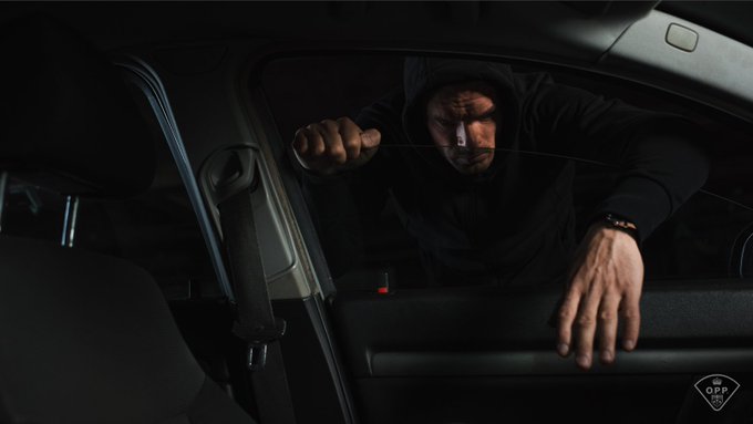 A thief in dark clothing reaches through a car window