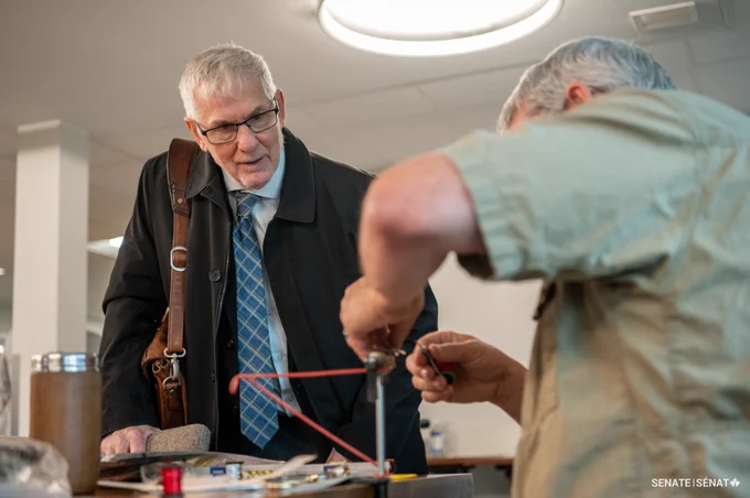 Senator David Richards leans in to watch a veteran make fly fishing lures.  