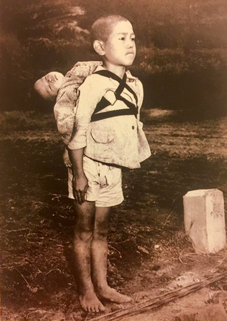 30. A Japanese boy waiting in line at the crematorium with his deceased baby brother on his back, Nagasaki, 1945.