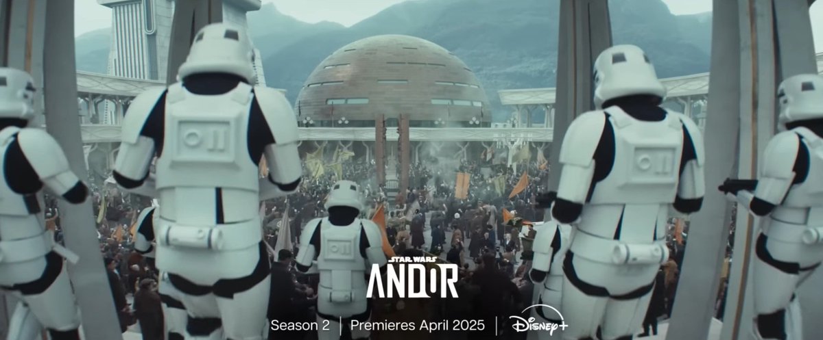 Another promo image, the same ad text at the bottom and the same golden dome, now centered in the frame and in front of some foggy green hills. The shot is over the shoulder of a half-dozen white armored Stormtroopers, descending steps into a crowd of warmly-dressed protesters holding banners aloft.