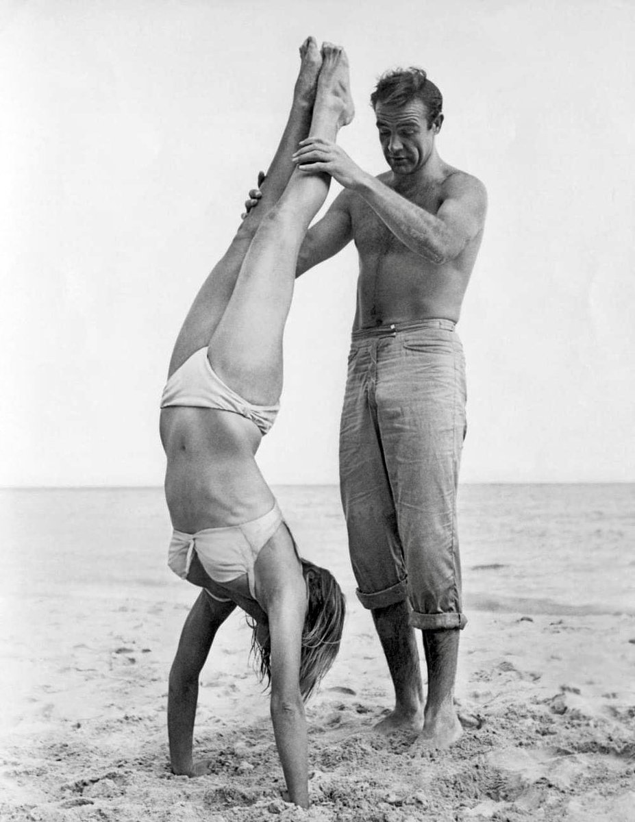 FilmsMap's tweet image. 1962: Shirtless Scottish actor Sean Connery holds Swiss actor Ursula Andress while she does a handstand on a beach in a white bikini on the set of the film, 'Dr. No'.