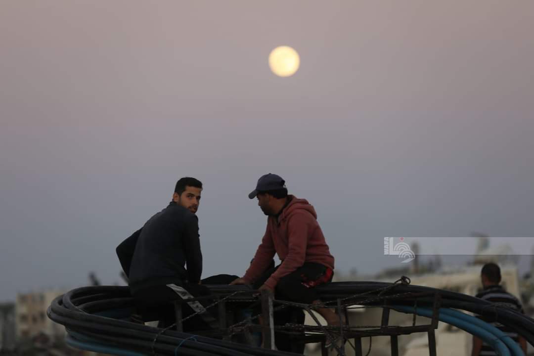 WAFANewsEnglish's tweet photo. Locals pose for pictures with the full moon  above the destroyed buildings in the town of Zawayda, central Gaza. https://t.co/QmizytsH4m