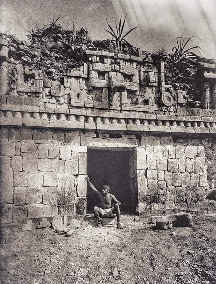 Persona posa bajo uno de los mascarones Witz (cerro) en la zona arqueológica de Xlapak, Yucatán. Zona Puuc, entre los sitios de Sayil y Labná. Año 1887.
