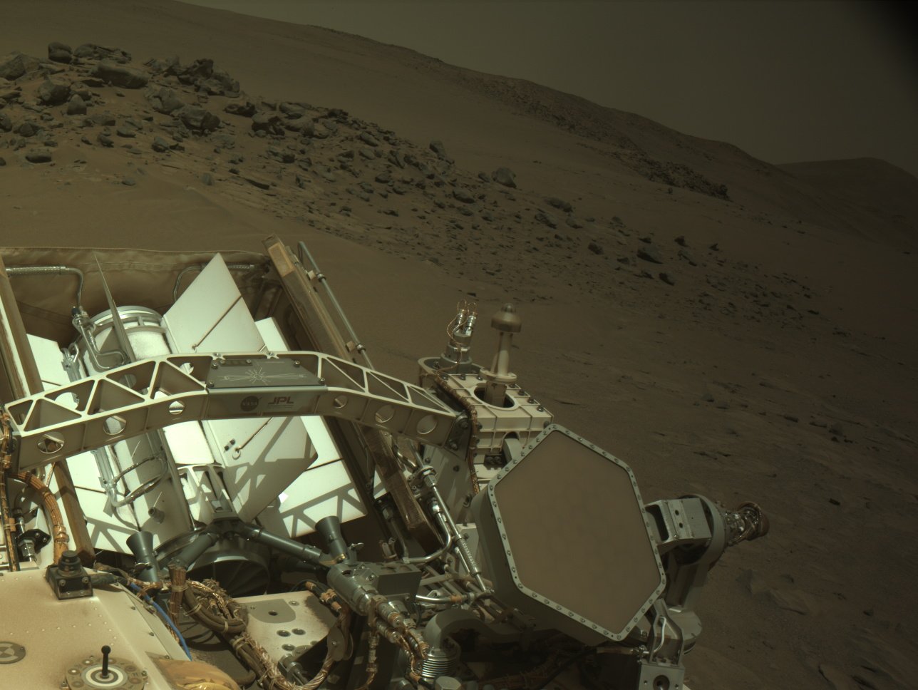 Part of the Perseverance Mars rover, including its hexagonal high-gain antenna, with the rocky, hilly deserts of Mars in the background