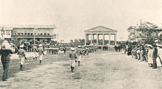 Cd. Guat. 1908.  Desfile escolar durante las Fiestas Minervalias en la Av. del Hipódromo, hoy Av. Simeón Cañas.  Al fondo el Templo a Minerva donde se realizaban los actos protocolarios. Se observan los niños con fusiles pues la educación estaba militarizada.