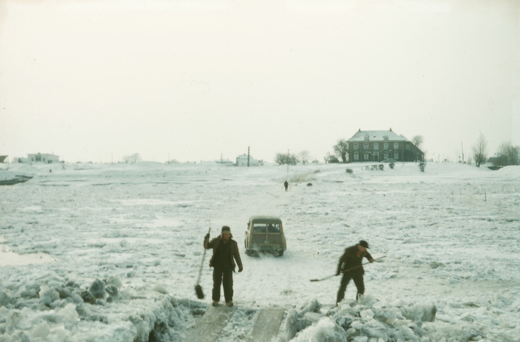 Een bevroren #Rijn rond februari in 1956. Bij één van de oudste Nederlandse veerponten, namelijk de #Opheusdense Veer, was er een pad gemaakt over het ijs, waarover men met de auto naar de overkant kon. (Bron: 0245-2739,Gelderse Komgrondencommissie, PDM 1.0 licentie)