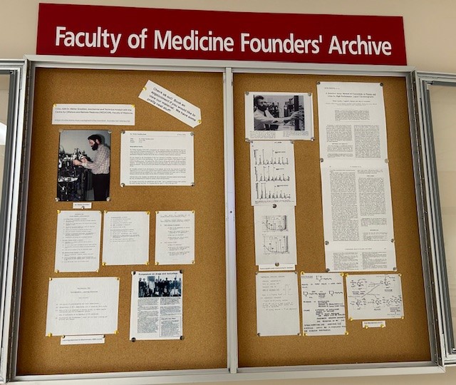 An open display case featuring photos and text pinned to a corkboard under a red sign that reads, "Faculty of Medicine Founders' Archive."