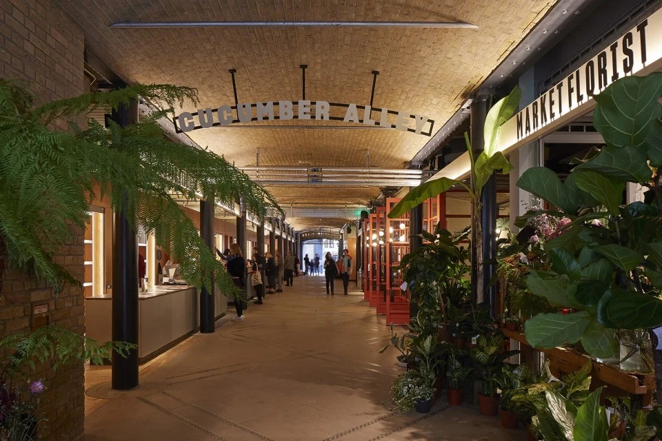 orientalli's tweet image. A bustling market area under an arched ceiling with stalls selling fresh produce and goods, adorned by a sign reading "Cucumber Alley
