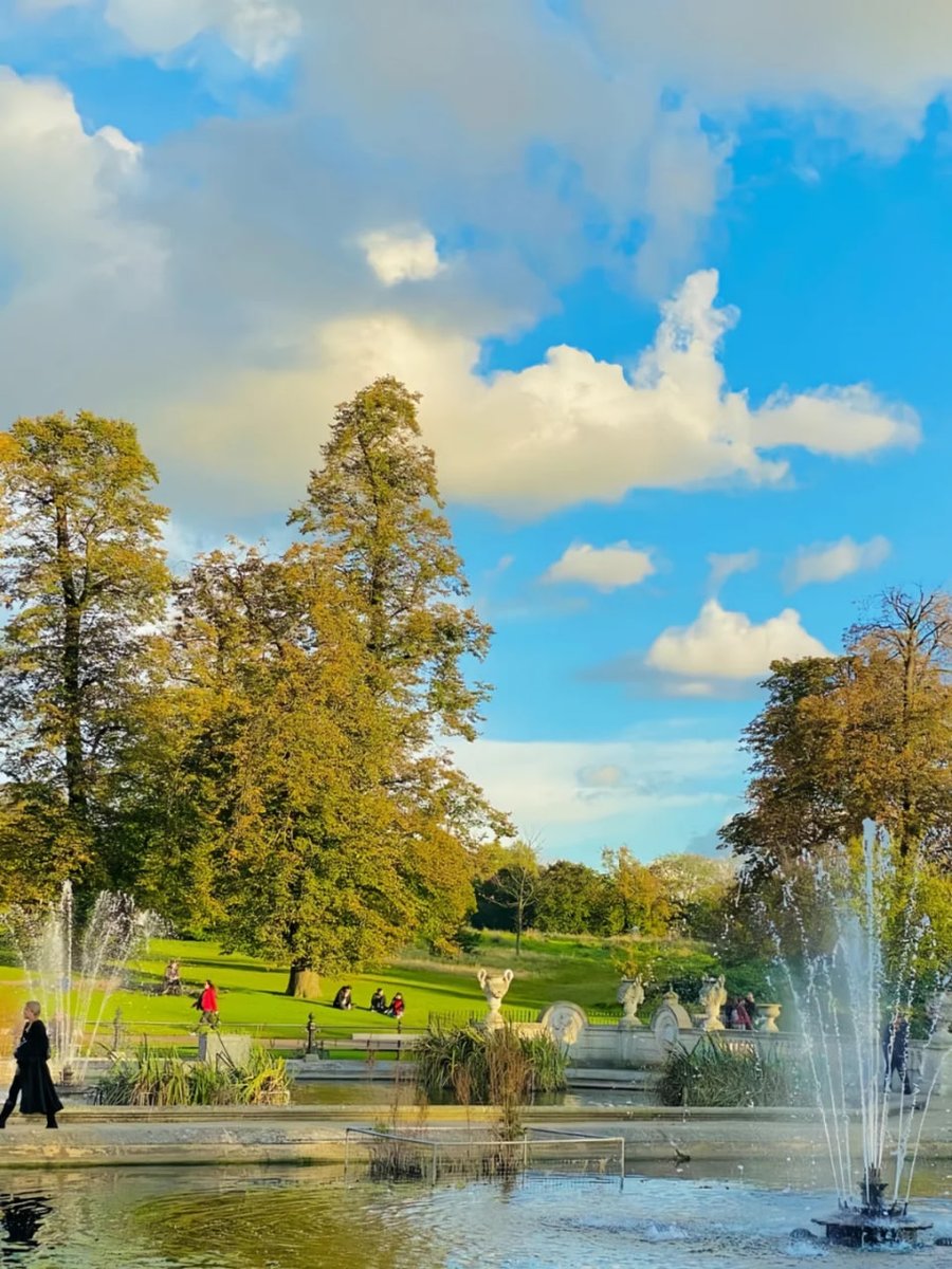 orientalli's tweet image. People enjoying a leisurely day on a grassy park, surrounded by blooming flowers and trees.