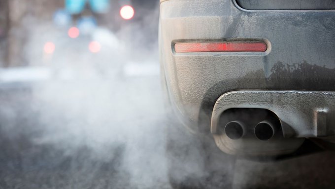 Close up photo of a car’s exhaust pipe with emissions coming out as the vehicle idles on the side of a street.