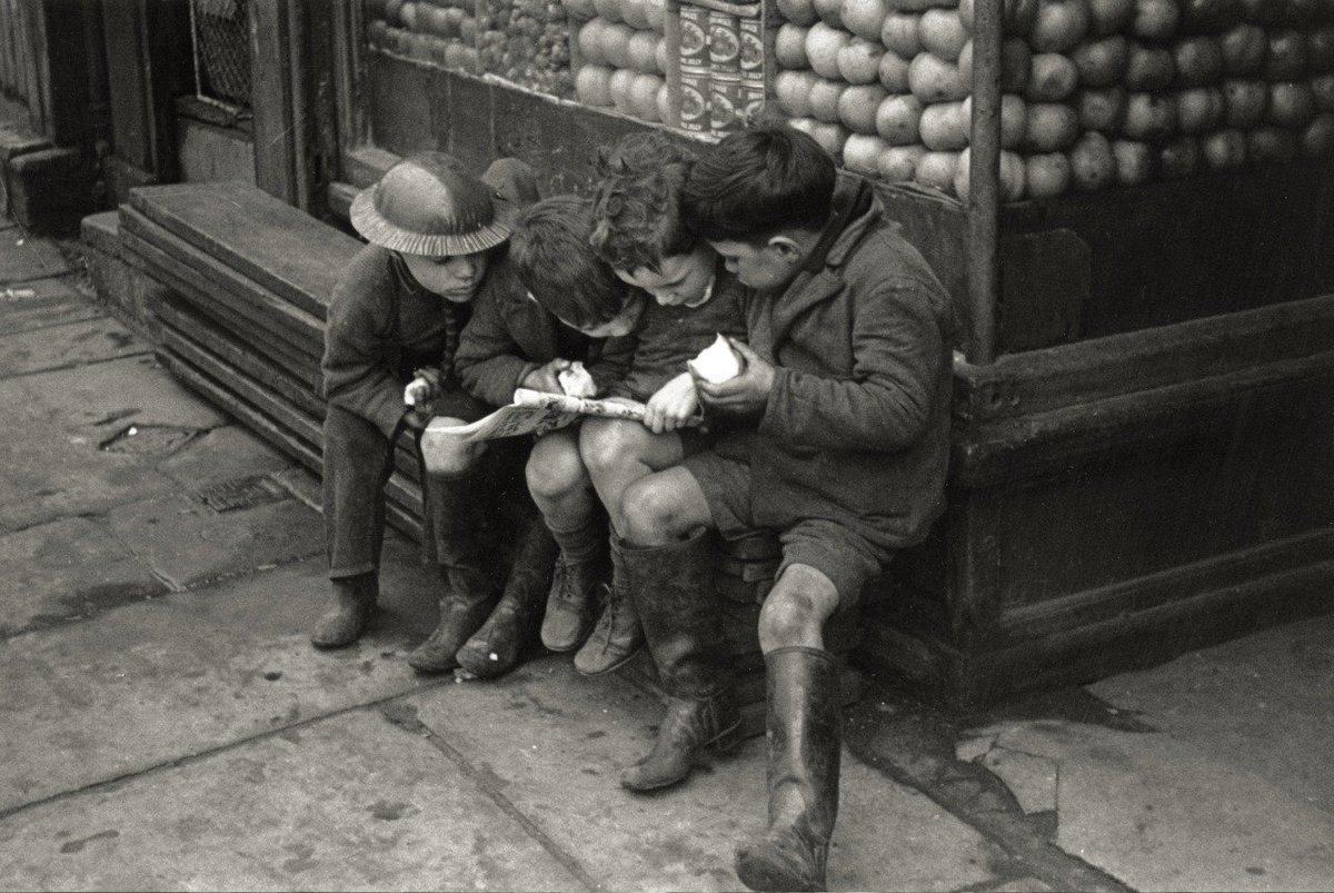 A boy in a tin hat hangs out with his friends outside a shop in Liverpool,1940’s - by Bert Hardy.