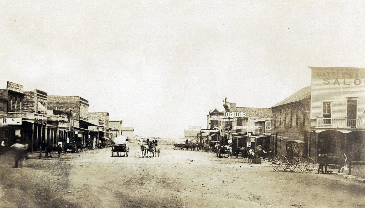 TracesofTexas's tweet photo. "Downtown" Abilene, Texas circa 1886. Being that Abilene was established in 1881, these buildings can't be more than a few years old. The building at the front right, The Cattle Exchange Saloon and Boarding House, was the first building in Abilene. It was built for the cattle drovers that passed through nearby. Frank and Walter Collins built this building, likely with money they earned as Texas Rangers in Company C of the Frontier Battalion. Walter died in his own room on the second floor, 45 minutes after an infamous January 1884 shooting affair in the saloon. Frank passed 2 months later at his home at the corner of 4th and Cedar, today where the Bee Hive Restaurant is located. This photo was taken from the train tracks looking North at North 1st and Pine.