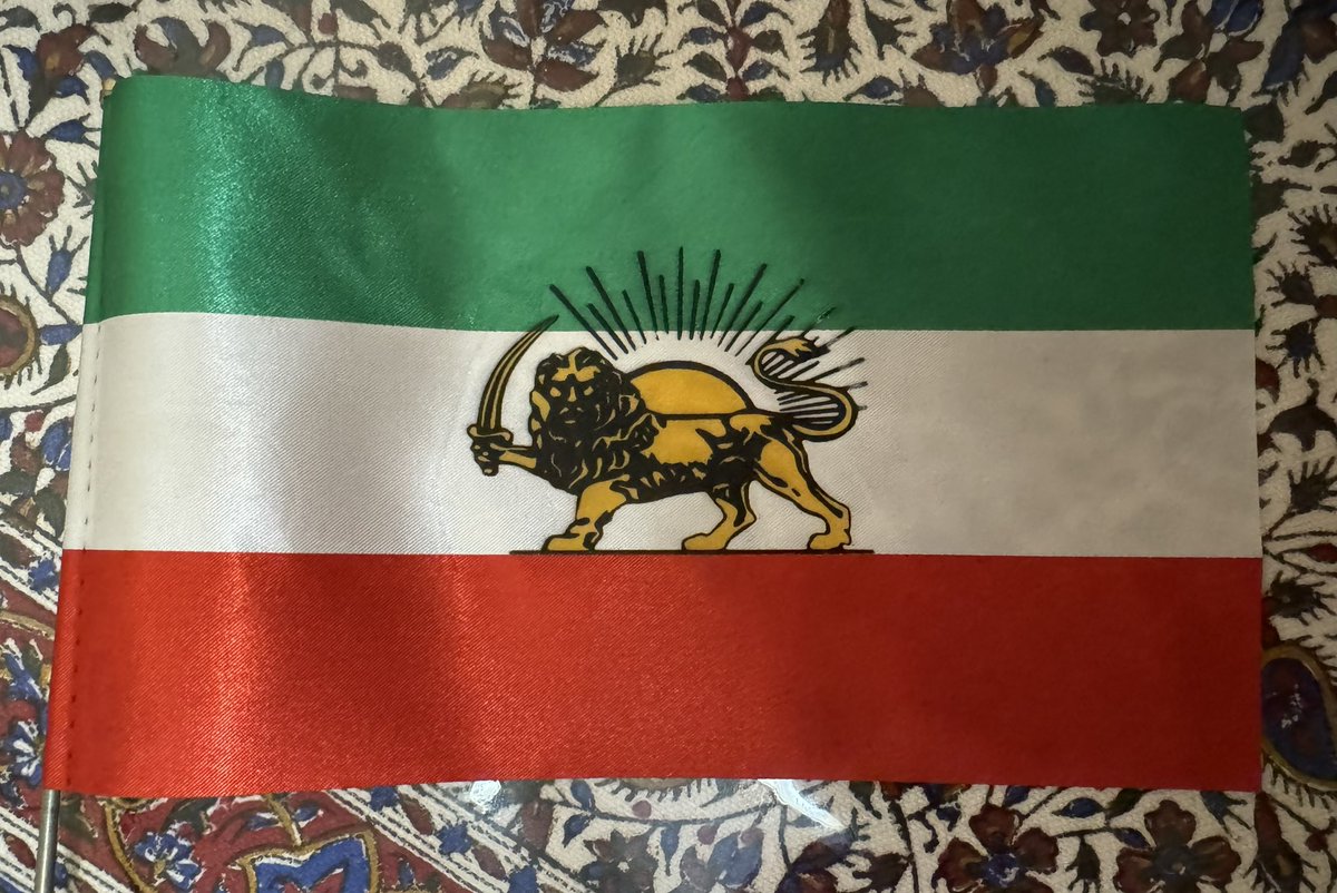 AfsaneyeRowshan's tweet photo. «آموزش دو روش ساده برای ساخت پرچم شیر و خورشید»
*** لطفا ریتوییت کنید تا همه ببینن و برای روزی که سالهاست منتظرشیم، آماده بشن***
در روش اول: 
نیاز هست به سه رنگ پارچه ترجیحا ساتن(برش خورده به اندازه مساوی)، کاغذ سابلیمیشن برای پرینتر معمولی/یا کاغذ چاپ تیشرت (برای رنگ روشن)، پرینتر رنگی (معمولا جوهرافشان) و اتوی خانگی. 
(قبل از طی این مراحل روی کار اصلی، مقداری از کاغذ را روی یه تیکه پارچه از همون جنس‌ امتحان کنید)
۱-طرح شیر و خورشید متناسب با اندازه پارچه سفید را بصورت برعکس mirror/flip با پرینتر رنگی(گفته شده در دستورالعمل کاغذتون) چاپ کنید. برای دو طرحی که شعاع خورشید فقط مشکیه، میتونید با ماژیک مشکی روی پارچه بکشیدش.
۲-دورتادور طرح شیر و خورشید را تا جایی که میشه قیچی کنید و بصورت برعکس در مرکز پارچه سفید قرار بدید و روی آن کاغذ روغنی(کاغذ شیرینی پزی/یا کاغذ معمولی سفید) بگذارید. دقت کنید که شمشیر باید سمت چپ که بعدا میله قرار می‌گیره، بیفته.
۳-اتو را در حالت غیربخار به داغ‌ترین حالت(۳۵۰ درجه) برسانید و روی طرح در حد سی ثانیه تا یک دقیقه بگذارید. اگر طرح بزرگ‌تر از سطح اتو هست، برای چند دقیقه اتو رو بطور مداوم همه جای طرح بکشید طوریکه همه جای طرح یک دقیقه حرارت خورده باشه.
۴-از چسب پارچه یا لایی چسب برای چسباندن پارچه سبز در بالا و پارچه قرمز در پایینِ پارچه سفید استفاده کنید یا تیکه‌ها‌ را به هم بدوزید. 
۵- قسمت لبه عمودی سمت چپ را به اندازه قطر میله فلزی یا چوب، به سمت داخل تا کنید و بدوزید، میله رو داخل پرچم قرار بدید و دو طرف رو با دوخت محکم کنید.
۶-اگر از پارچه ساتن استفاده کردید، دور تا دور پرچم را فندک بگیرید تا بسوزه و مانع ریش ریش شدن پارچه بشه.
دستور چاپ روی پارچه رو مطابق با دستورالعمل کاغذ خودتون که میگیرید، پیش ببرید.
«روش دوم»: نقاشی به جای پرینت:
در این روش پارچه مناسب برای رنگ آمیزی را انتخاب کنید، با کاربن طرح شیر و خورشید را وسط پارچه سفید منتقل کنید، و خطوط را با ماژیک مشکی پررنگ کنید. داخل طرح را رنگ زرد بزنید؛ بعد از خشک شدن رنگ زرد، دوباره خطوط مشکی را پر رنگ کنید تا اگر رنگ زرد روی خط‌ها رو گرفته، طرح صاف و منظم بشه.
بقیه مراحل با روش اول یکسان هست.
به جای کاربن، برای انتقال طرح و برای مرحله نهایی پررنگ کردن خطوط مشکی، میتونید صفحه نور(گوشی یا تبلت با نور زیادش) و طرح را زیر پارچه بگذارید و با واضح شدن خطوط، طرح رو بکشید.
اگه سوالی داشتید حتما پیام بدید.
#ایران_معبد_ماست