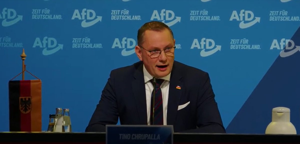 scheunert's tweet photo. Warum nutzt die #AfD bei der Ernennung von #Weidel als #Kanzlerkandidatin anmaßender- sowie verbotenerweise die Bundesdienstflagge in Bannerform? Die miserable Ausleuchtung vor Ort und die absurd deplatzierte Kaffeekanne ist da schon eher das passende Niveau der Rechtsextremen. https://t.co/ZEmUxnKtA0
