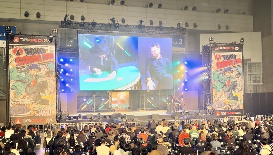 Leo6969's tweet photo. 東京コミコン2024
控えめに言っても最高でした‼︎

ジュード・ロウ、マッツ・ミケルセン、ベネディクト・カンバーバッチをはじめ地上にこれほど豪華な空間が存在するのかとため息がでるようなハリウッドセレブたちの饗宴！
特に今回の東京コミコンはポップカルチャーの祭典銘打ってありとあらゆるジャンルやアート、エンターテインメントが次から次へとステージを彩りました。
どのアーティストやパフォーマーも素晴らしく、ステージで繰り広げられる極上のエンタメに目が釘付けでした👀
そんな中、私たちマジック勢はフィナーレ前の言わばトリとも言えるポジション。
私は正直ハリウッドセレブや他のパフォーマーのファンの目に我々のパフォーマンスがどう映るのか、いくばくかの不安がありました。
しかし！
まさにマジック界のアベンジャーズのような我らがスターマジシャンたちは圧巻とも言うべき最高のパフォーマンスを見せてくれたのです‼︎
SHINGOの得意の風船パフォーマンスはマジック慣れしていない観客に大きな衝撃を与え驚嘆と称賛の的になっていました。
続いて登場したKiLaさんは、タレントの関根ささらさん相手にカードのインポッシブル ロケーションと客席から選ばれたお客さん相手にピックポケットの実演をしました。
これがまた演出がクールでカッコいいんだわ！
思わず隣りにいたトゥレーンに「KiLaさんカッケー‼︎」と叫んでしまったほどです😆
そして我らが高橋匠は何とあの！ダニエル・ローガンをテーブルに招いて超絶カードマジックを披露！
昨日まで体調不良でグダっていたのが嘘のようにキレキレなカードテクニックを披露しました。ダニエル・ローガンのリアクションを観れば彼がどれほどの衝撃を受けたか想像に難く無いでしょう。我々身内スタッフはみな「匠さんて何でステージに立つと別人のようにキラッキラのスーパースターに変身するんですかね？」と口を揃えて不思議がっていました。
そしてそして！ついにあのプリンセス天功さんが降臨しました‼︎
自分でキャスティングしていながら実際に華麗なイリュージョンで登場した瞬間には「プリンセス天功さん本当に出てくるんだ！」と感激してしまいました🤣
プリンセス天功さんはVRライブペインターのせきぐちあいみさんとコラボした圧巻のパフォーマンス！
ド派手な衣装チェンジにはじまり、息を呑む緊迫のイリュージョンショー‼︎
最高すぎました！いやあまりに凄すぎました。その存在感はハリウッドセレブにも負けていないくらいの強烈なオーラを纏っておりました。

東京コミコンに参加した全てのアーティストやパフォーマーは素晴らしかった。
惜しみない称賛とリスペクトを送りたいです。
しかしながらマジックは
マジシャンたちは
どのパフォーマーたちにも全くひけをとらなかったと証言をしておきます！

本当にカッコ良かった！
本当に素晴らしかった！
私はマジックに携わっていてこんなに誇らしいと思ったことはないです‼︎

ブースエリアで行われたクロースアップマジックも毎回毎回立ち見で溢れるほどの超満員。
出演してくれたマジシャンたちのレベルの高さは、初めてマジックに触れる人もいるであろう東京コミコンの観客に、マジックのイメージを根こそぎひっくり返されるような驚きと感動を与えたに違いありません。
ショーを観たあとのお客さんの笑顔や感想を聞いて、好評だったマジック教室も含めてブース内でのイベントも大成功であったことも報告しておきます。

それから最後に。
マジックショーのためにわざわざ幕張メッセまで応援に駆けつけてくださった
オズマンドの常連の皆様、
各マジシャンのファンの皆様、
本当に本当にありがとうございます！🙇‍♂️
ハリウッドセレブお目当てに来られるお客様が大半のこの東京コミコンで、暖かく迎えて貰いながらも心境的には我々正直かなりアウェイでした（笑）
そんな中、観客席に陣取って声援を送ってくださったことがどれほど心強かったか🙏ブースエリア、メインステージ共にこれほどの反響をいただき大成功出来たのも、
ひとえに見覚えある皆様💕の声援
あってのことだと心から感謝申し上げます‼︎
チーム『マジック』の結束力を目の当たりに出来た気持ちでした‼︎
本当に本当にありがとうございますした！⭐️

#東京コミコン2024
#マジックフェスティバル