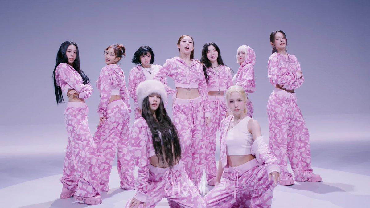 A promotional photo of the K-pop group fromis_9 wearing matching pink camouflage tracksuits against a light background, with Korean text at the bottom reading 'fromis_9' and '9 fromis.'