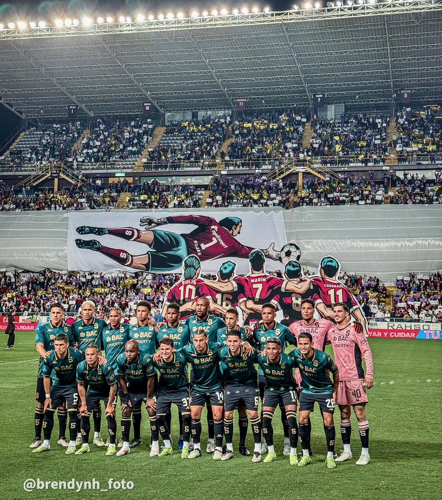 presimorado's tweet photo. Esta foto es tan interesante en tantos niveles que es casi perfecta 🤩 . Los 5 puntos clave que resalto:

✅ Tifo “movil” de Marco Antonio Rojas, homenajeado, mostrando cómo el arquero histórico “vuela” hacia el balón
✅ Abajo del tifo de Marco Rojas hay un segundo tifo de los 5 ídolos que ya estaban con sus camisas en el techo, todos abrazados viendo a don Marco y dándole la bienvenida al nuevo integrante del exclusivo club 
✅ Arriba a la izquierda se ve la nueva camisa colgada de Don Marco, una layenda más en lo más alto de La Cueva 
✅ El equipo se toma la foto con todos los jugadores (titulares y banca) abrazados en muestra de unión, lo cual ha sido tradición en los últimos torneos
✅ Los jugadores usando el nuevo uniforme que es simplemente fuera de serie, en homenaje a los grandes arqueros del club

En fin, un momento sencillamente épico que queda recogido en una fotografía para la posteridad. Una noche mágica más en La Cueva 

📷 @NunezBrendy
