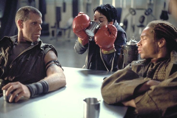 Annalee Call trying to drink Johner's moonshine with boxing gloves as Christie watches. Ron Perlman, Winona Ryder, Gary Dourdan. "Alien:Resurrection" 1997.