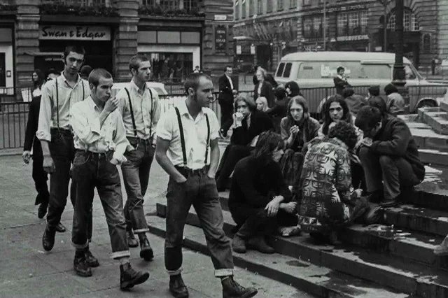 Piccadilly Circus, London, 1969, a group of skinheads walk past a group of hippies