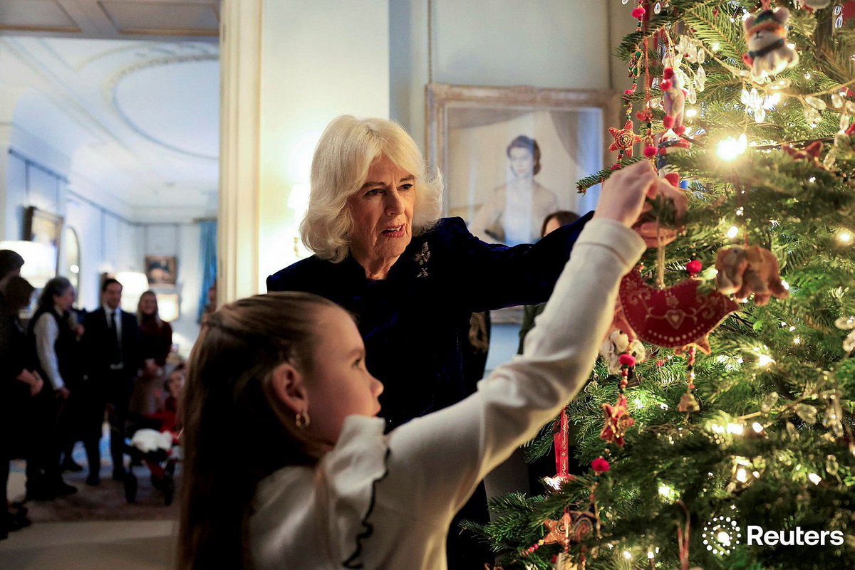 Britain's Queen Camilla helps a child hang a decoration on a Christmas tree, as she meets parents and children supported by Helen &amp; Douglas House and Roald Dahl's Marvellous Children's Charity, at Clarence House in London photo by <a href="/minakim_01/">mina</a> for REUTERS